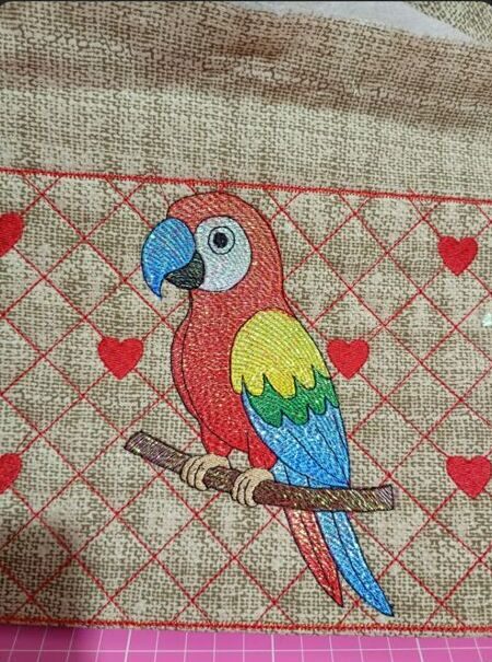 Necessaire com bordado de uma arara colorida sobre fundo de corações vermelhos